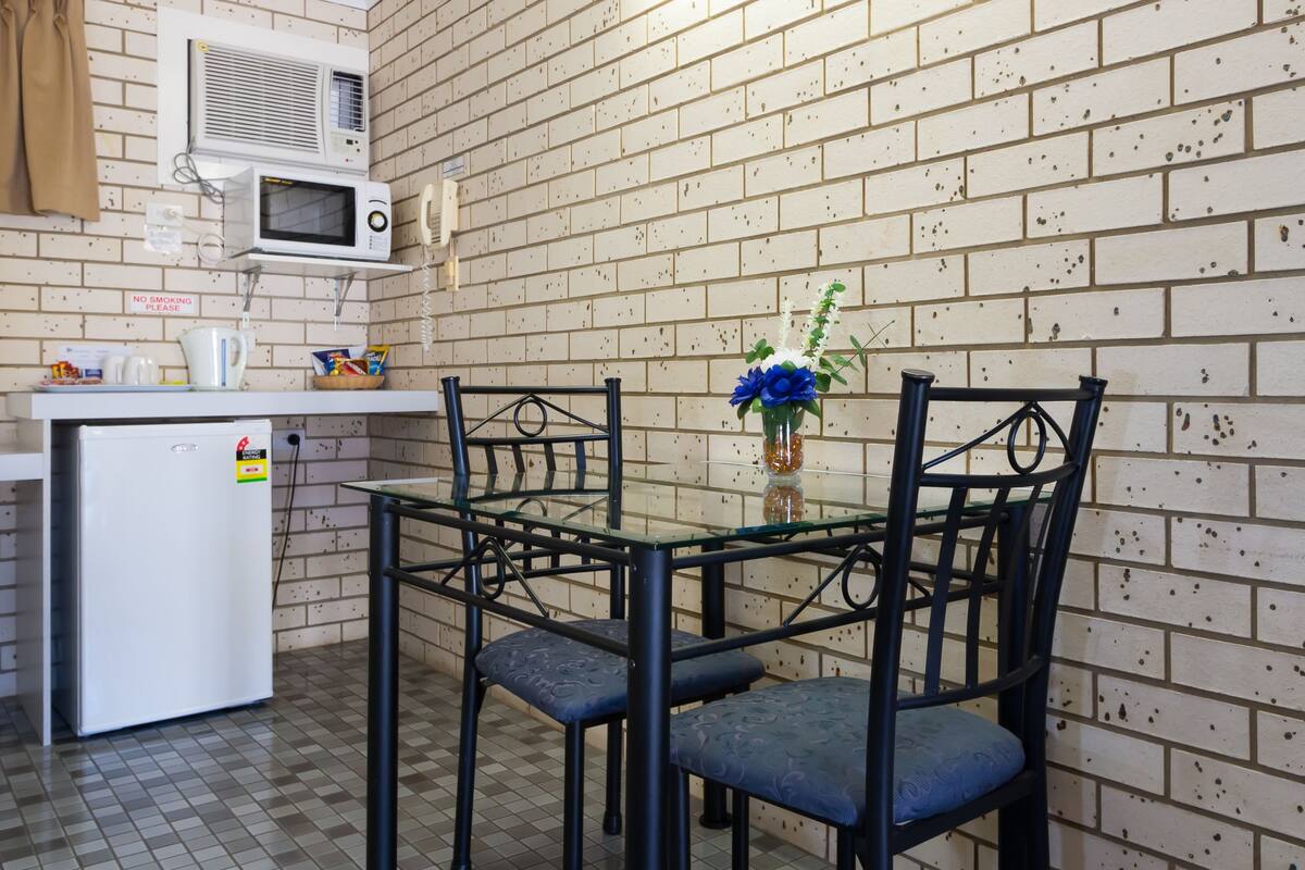 A compact kitchen with a microwave, a small refrigerator, and a glass table with chairs.