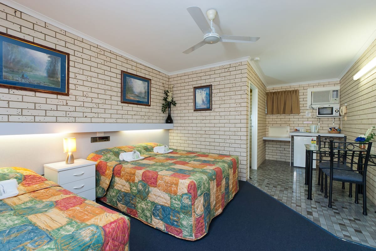 A room with two beds, a desk, a chair, a ceiling fan, and a microwave.