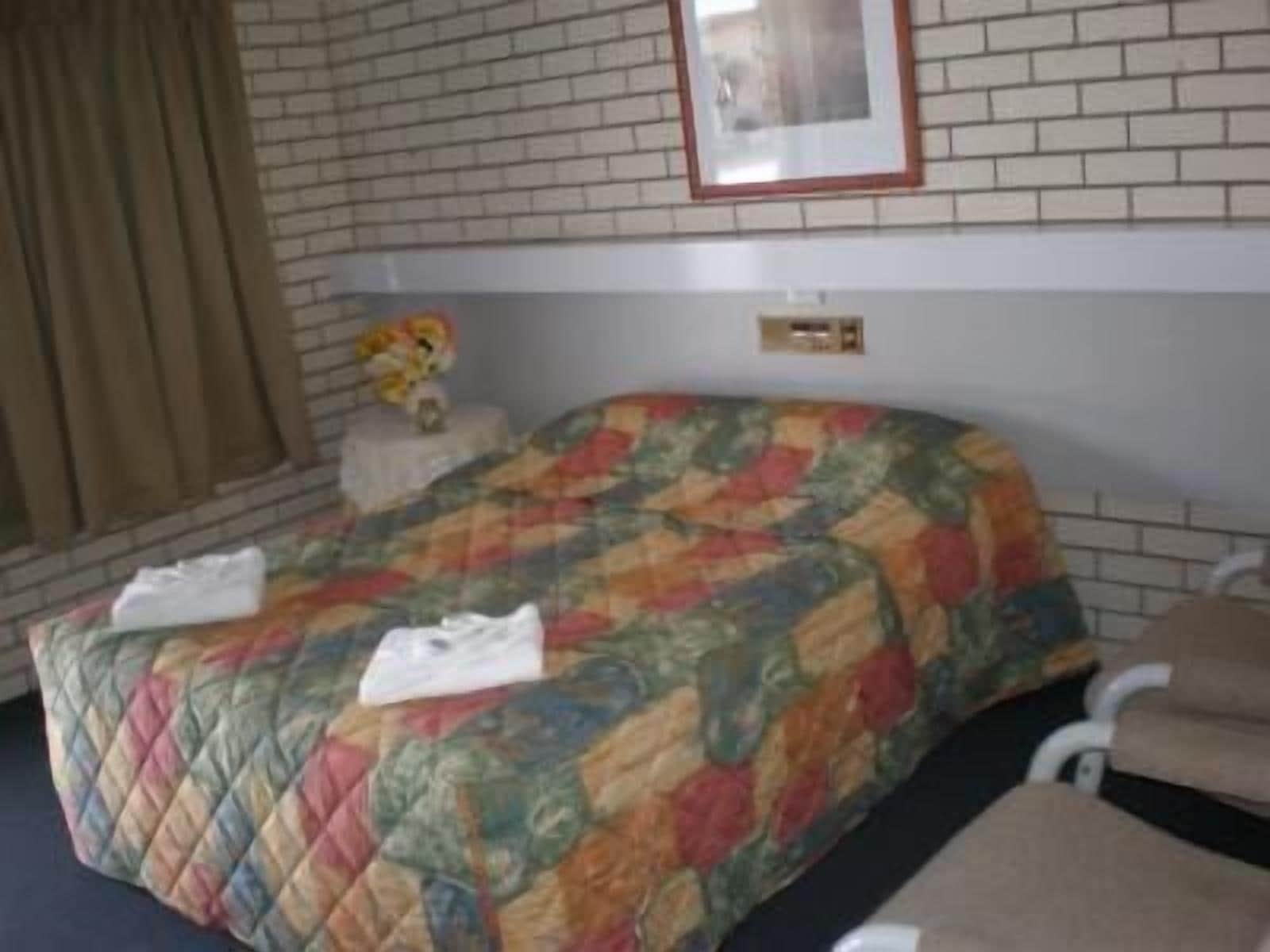 Een hotelkamer met een gewatteerde spreideken, een wit hoofdeinde, een inlijsting afbeelding aan de muur en een raam met gordijnen.