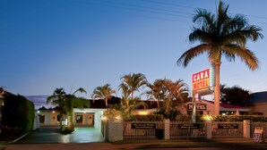 Un motel con una palmera, un letrero que dice "CARA MOTEL" y una entrada con portón.