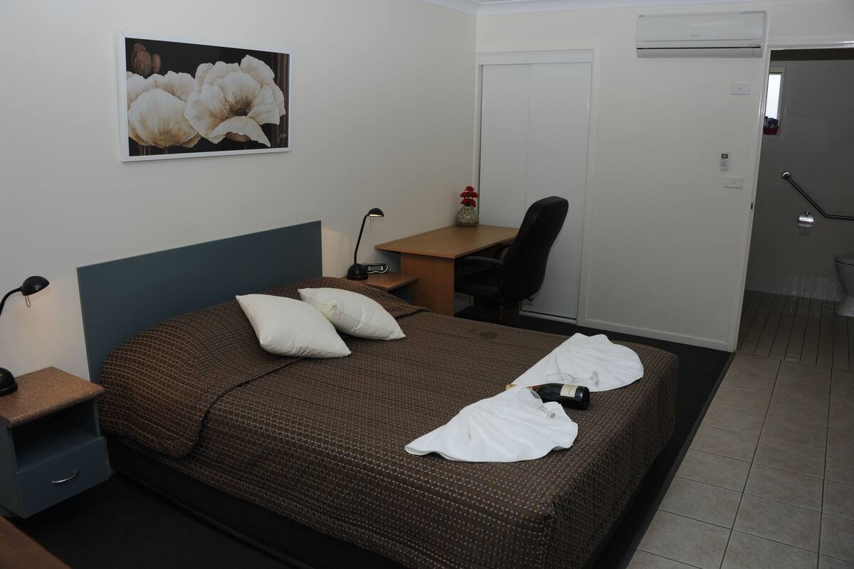 Ein Hotelzimmer mit Bett, Nachttisch, Lampe, Stuhl, Schreibtisch und einer Tür.