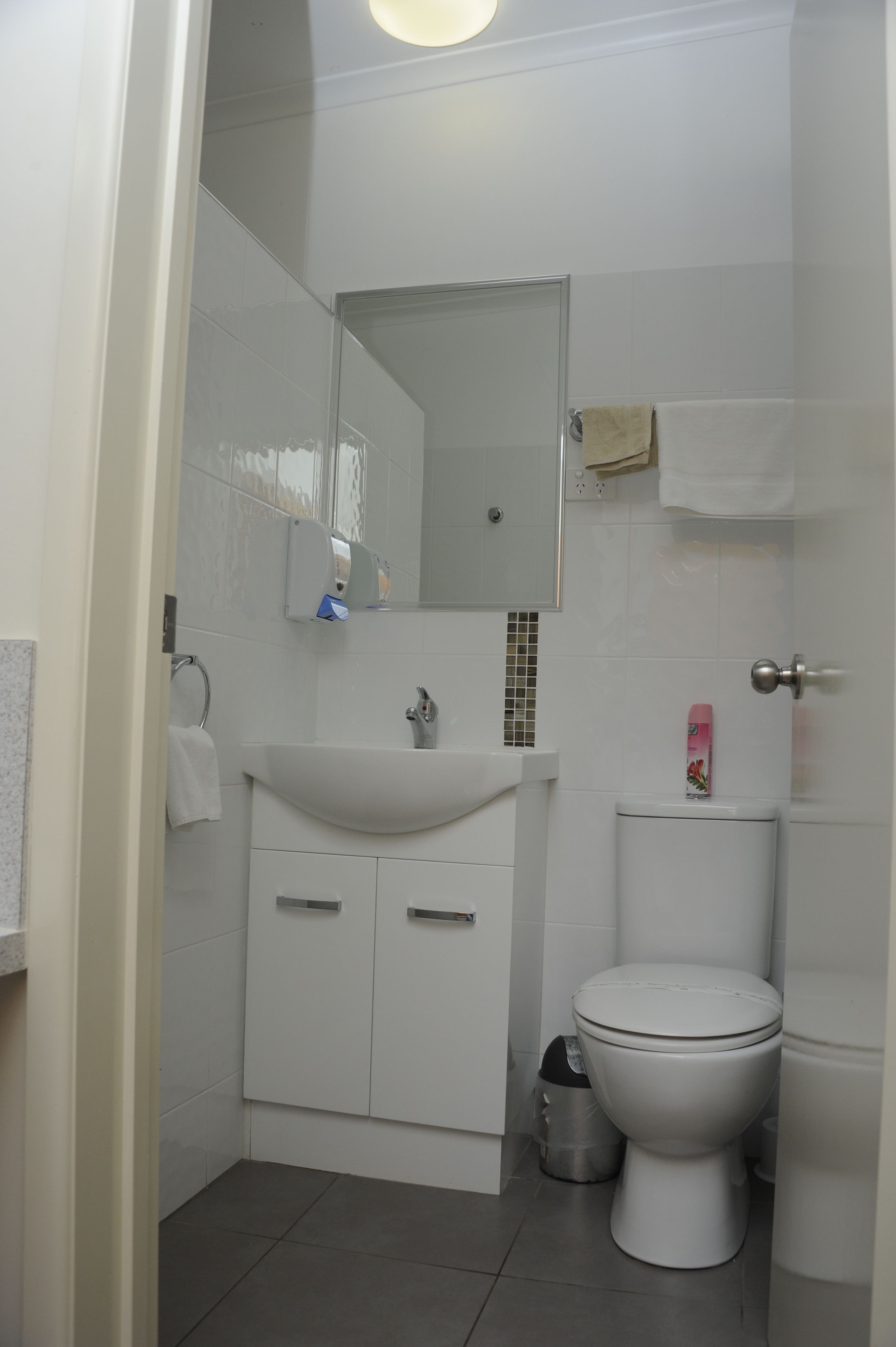 A small, modern bathroom with a white sink, mirror, and toilet.