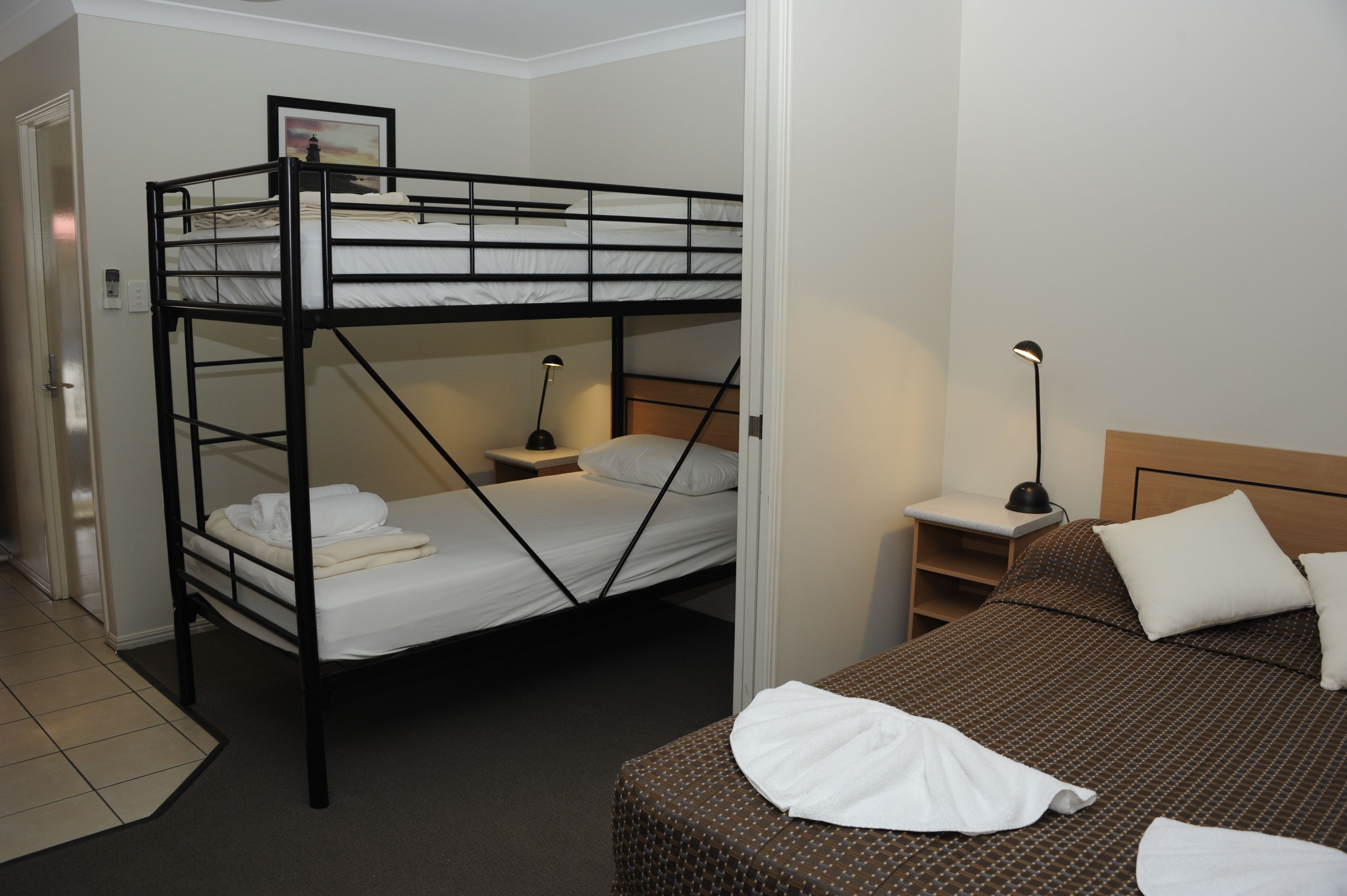 A bunk bed room with a desk and chair, a bedside table with a lamp, and a bed with a patterned bedspread.