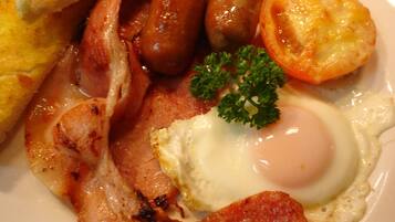A plate of breakfast food including sausages, bacon, a fried egg, toast, and a tomato.