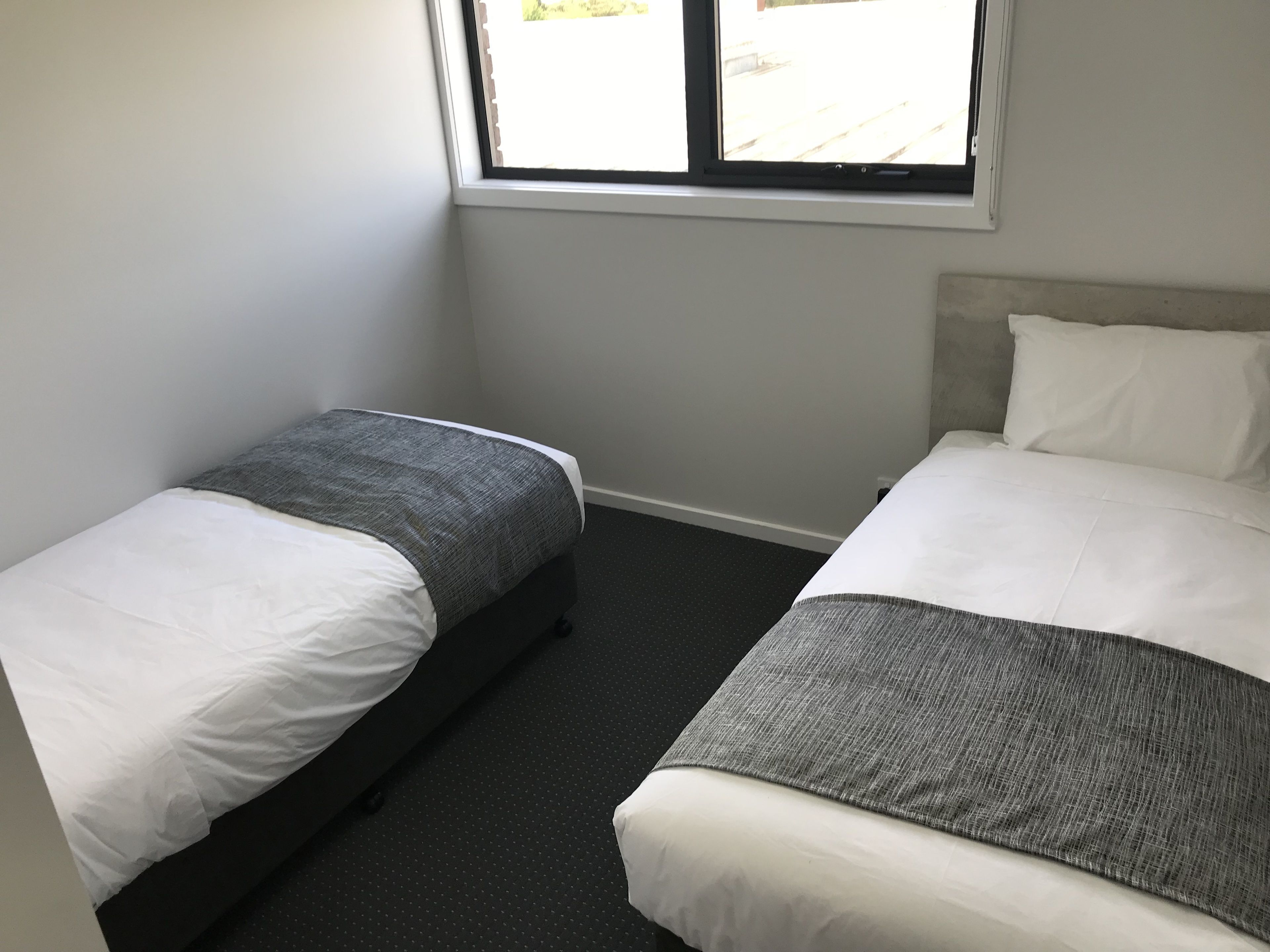 A room with two beds, one with a grey bedspread and the other with a white bedspread.