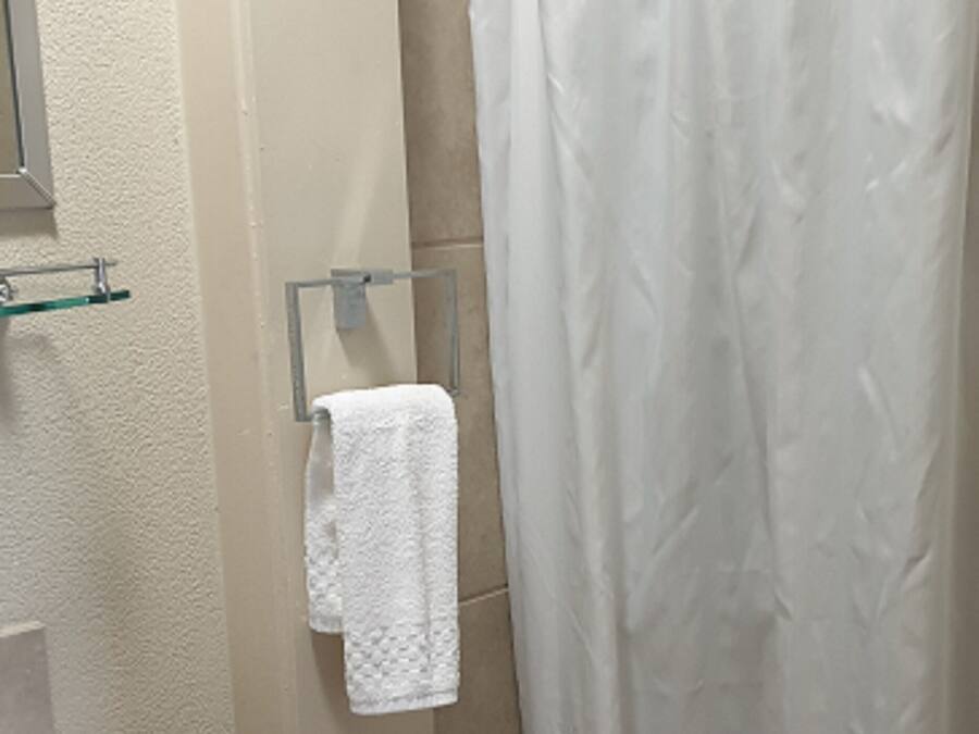 Een badkamer met een wit wastafel, een glazen plank, een handdoekhouder met een witte handdoek en een douchegordijn.
