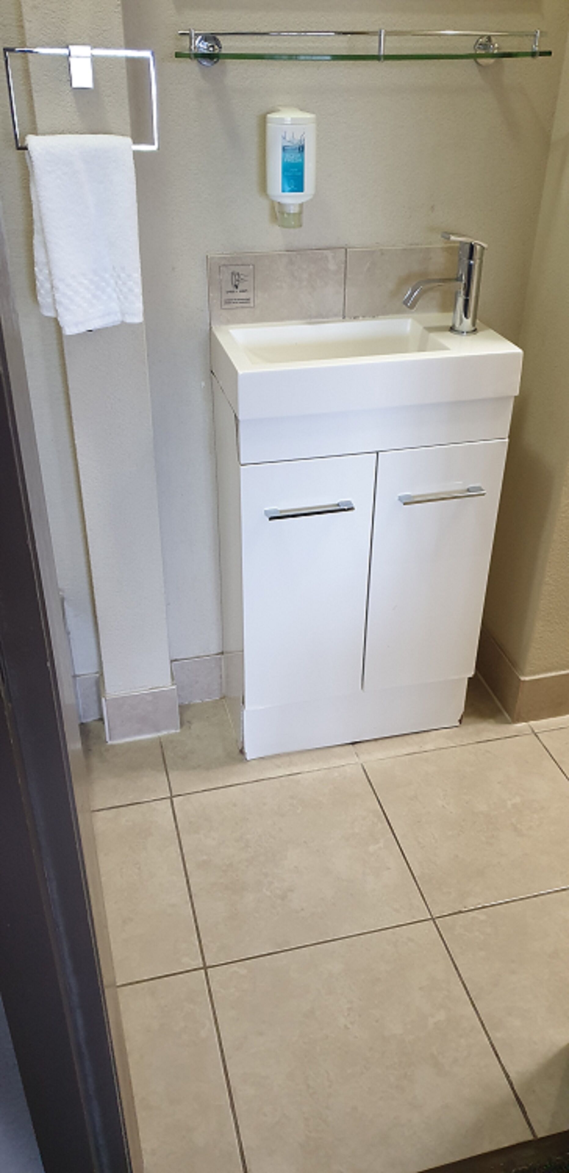 Un baño con un lavamanos blanco, dos armarios, un perchero y un dispensador de jabón.