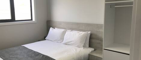 A bedroom with a bed, a nightstand, a wardrobe, and a window.