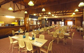 A spacious dining area with multiple tables and chairs, wooden beams on the ceiling, and a bar area with a menu board. - Seabrook Hotel (Somerset)