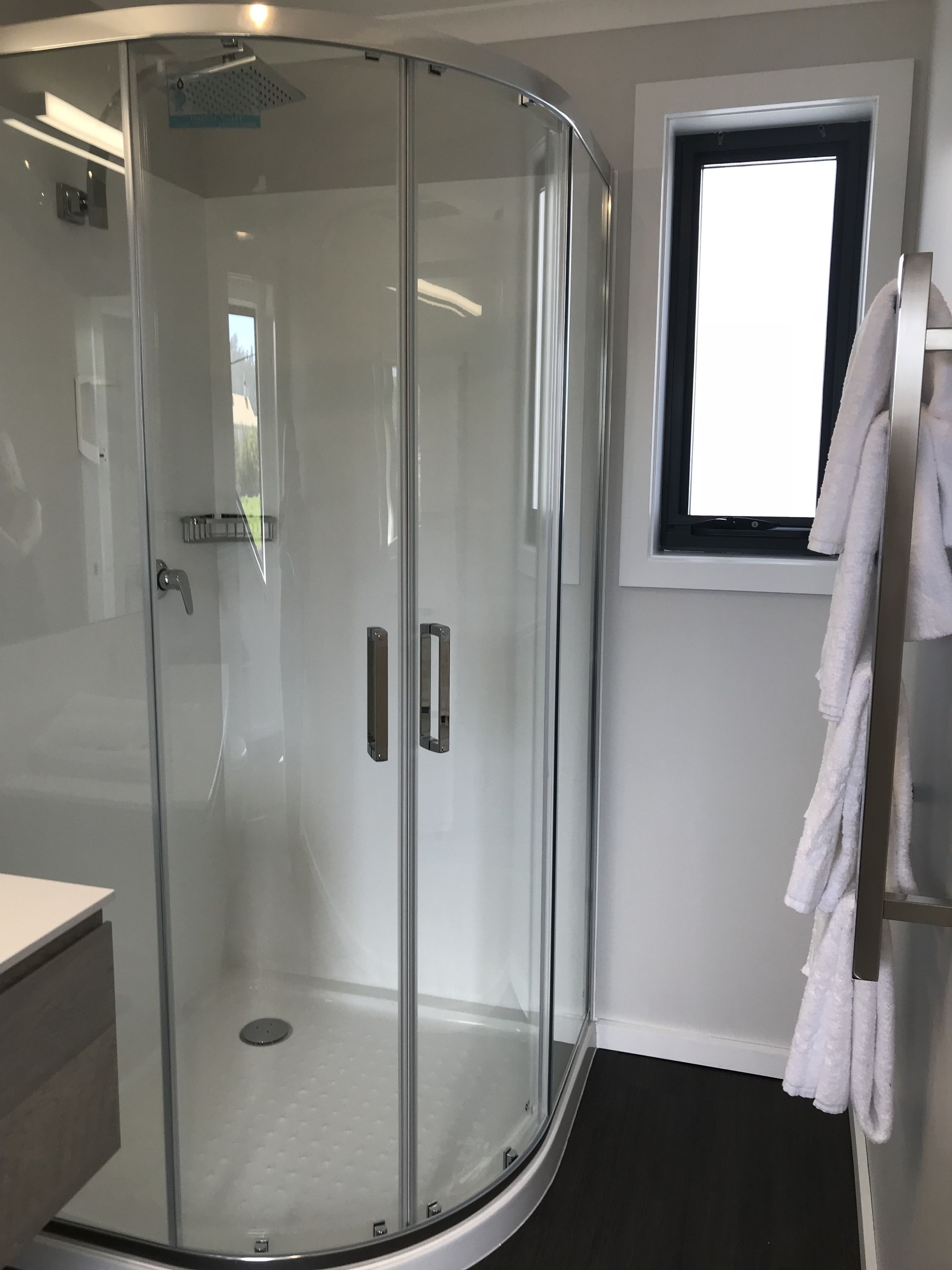 Un baño moderno con ducha de vidrio, lavamanos blanco y ventana que proporciona luz natural.
