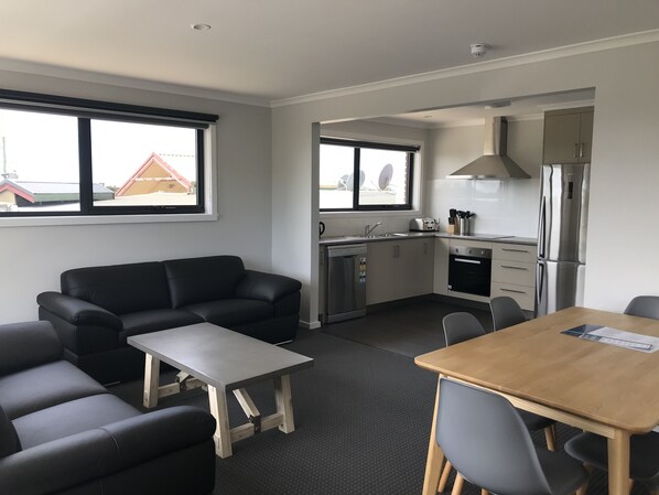 A modern living room with a black leather sofa, a wooden coffee table, and a dining table with chairs. - Seabrook Hotel (Somerset)