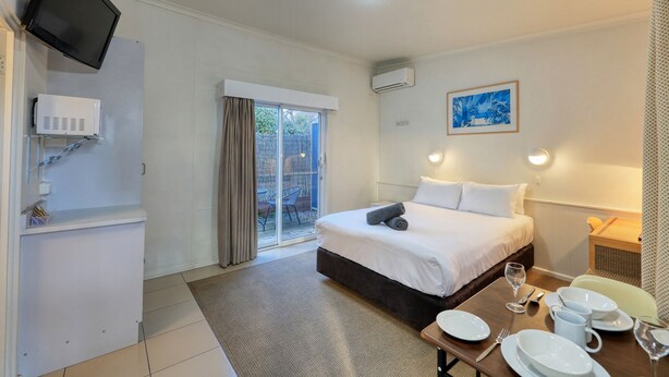 Habitación de hotel con cama, una mesa de comedor con platos y vasos, un televisor montado en la pared y una ventana con cortinas.