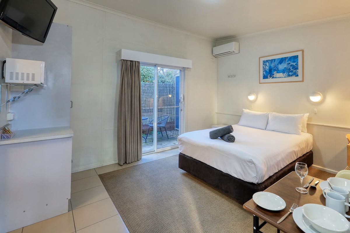 A hotel room with a bed, a dining table set with plates and glasses, a TV mounted on the wall, and a window with curtains.