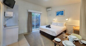A hotel room with a bed, a dining table set with plates and glasses, a TV mounted on the wall, and a window with curtains.