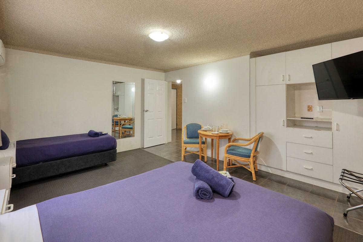 A hotel room with a large bed, a desk with a chair, a television, and a wardrobe.