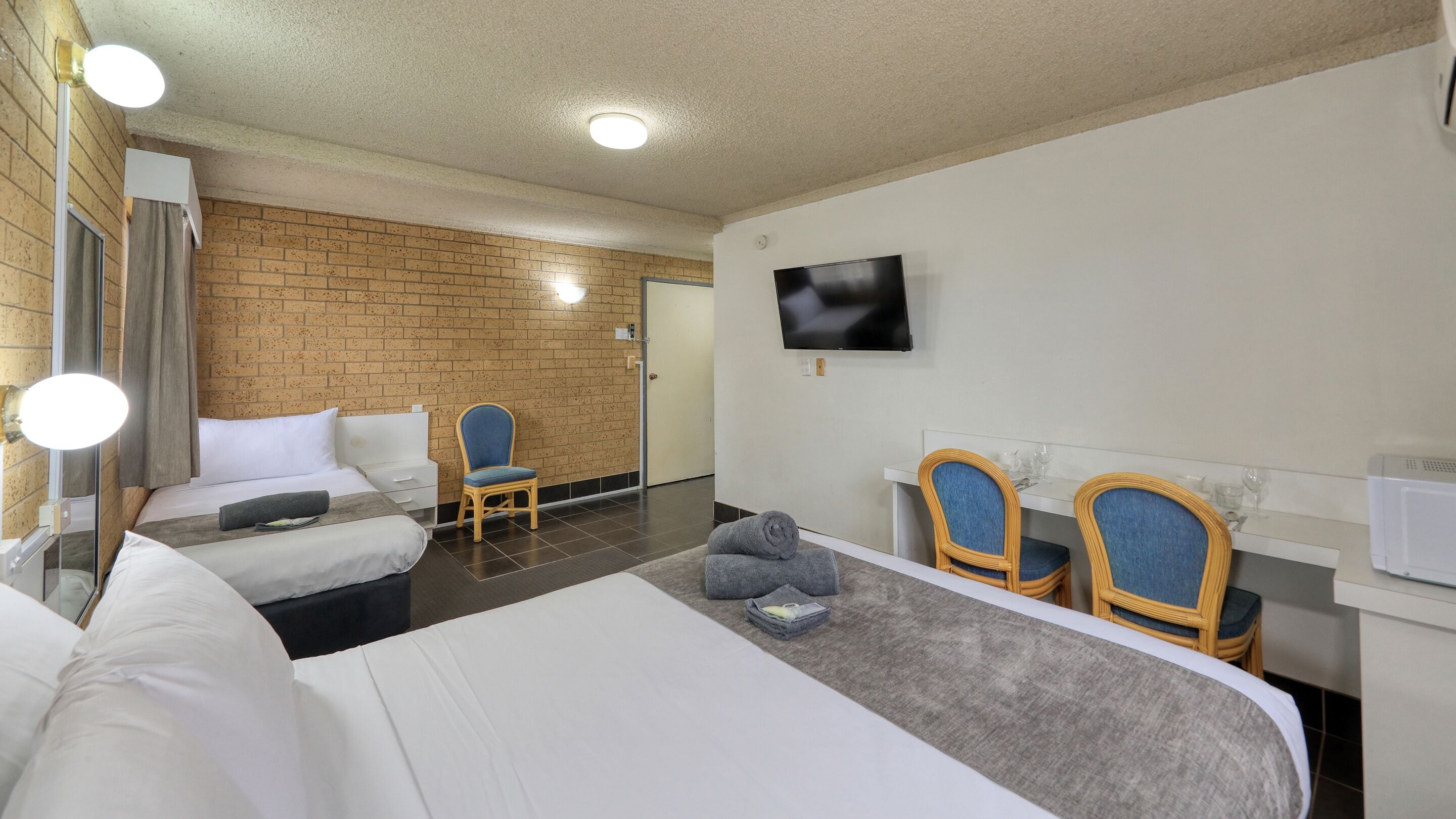 A hotel room with a bed, a chair, a TV, and a small table with glasses and a microwave.