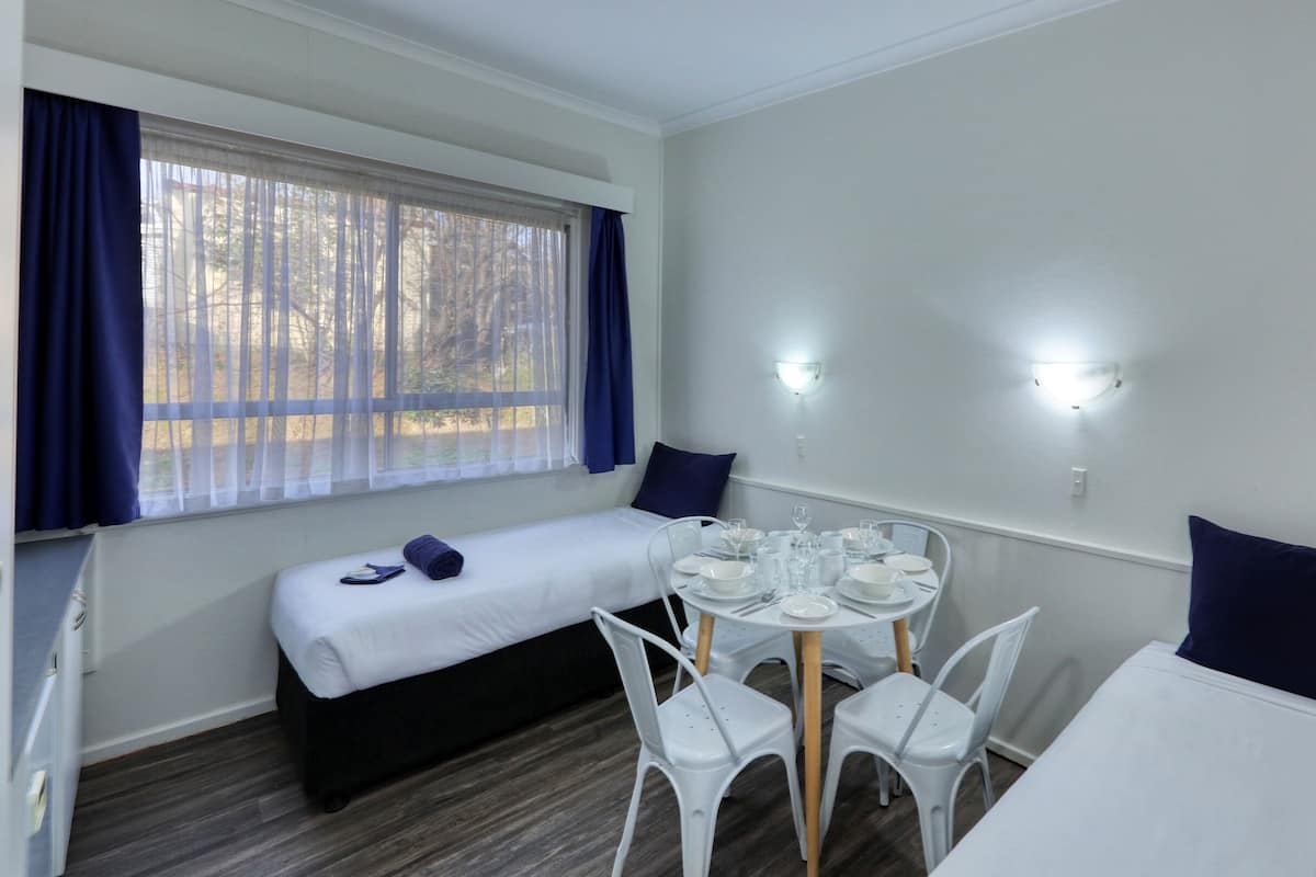 A room with a bed, a dining table set for four, and a window with curtains.