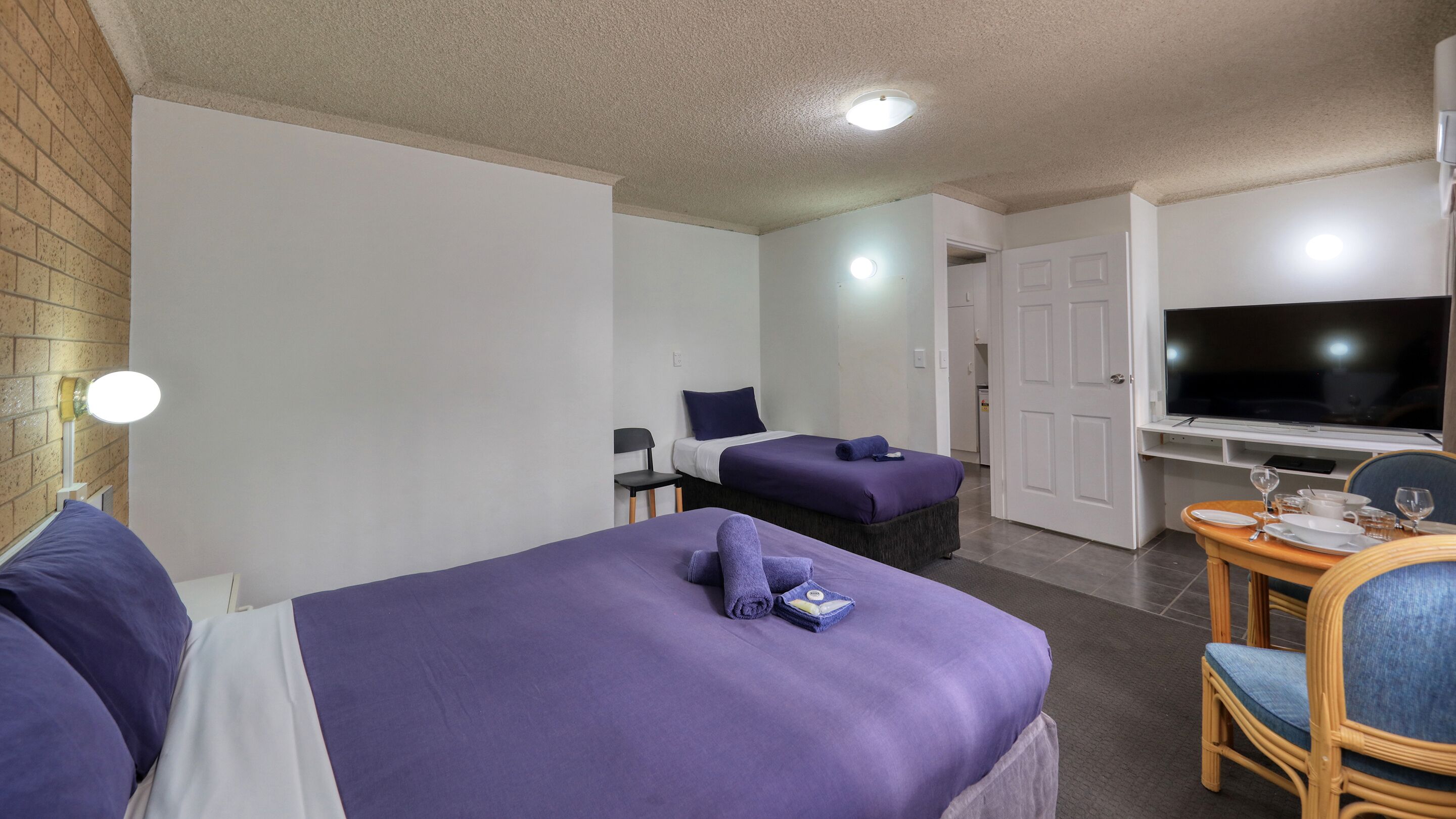 A hotel room with two beds, a television, a dining table with chairs, and a small desk.