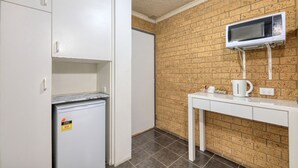 Una kitchenette compacta con refrigerador, microondas y una mesita con tetera y taza.