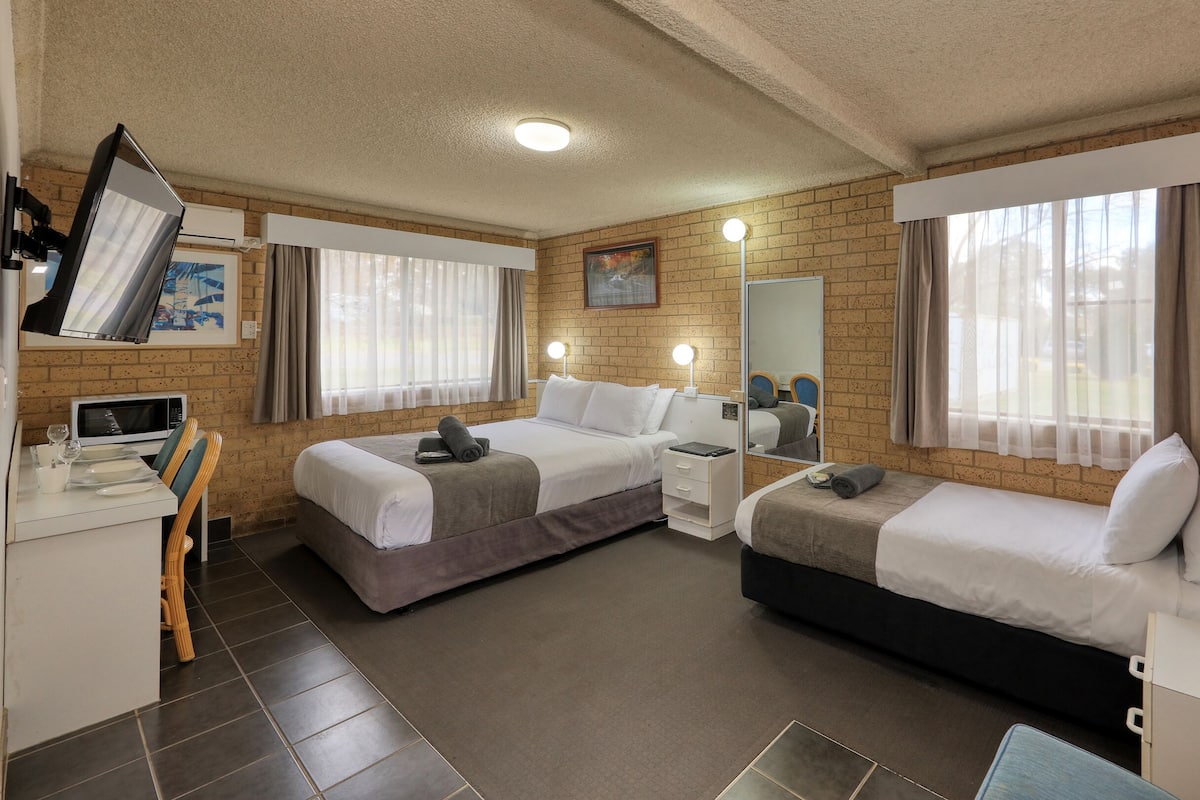 A hotel room with two beds, a desk with a computer, a microwave, and a dining area with chairs.