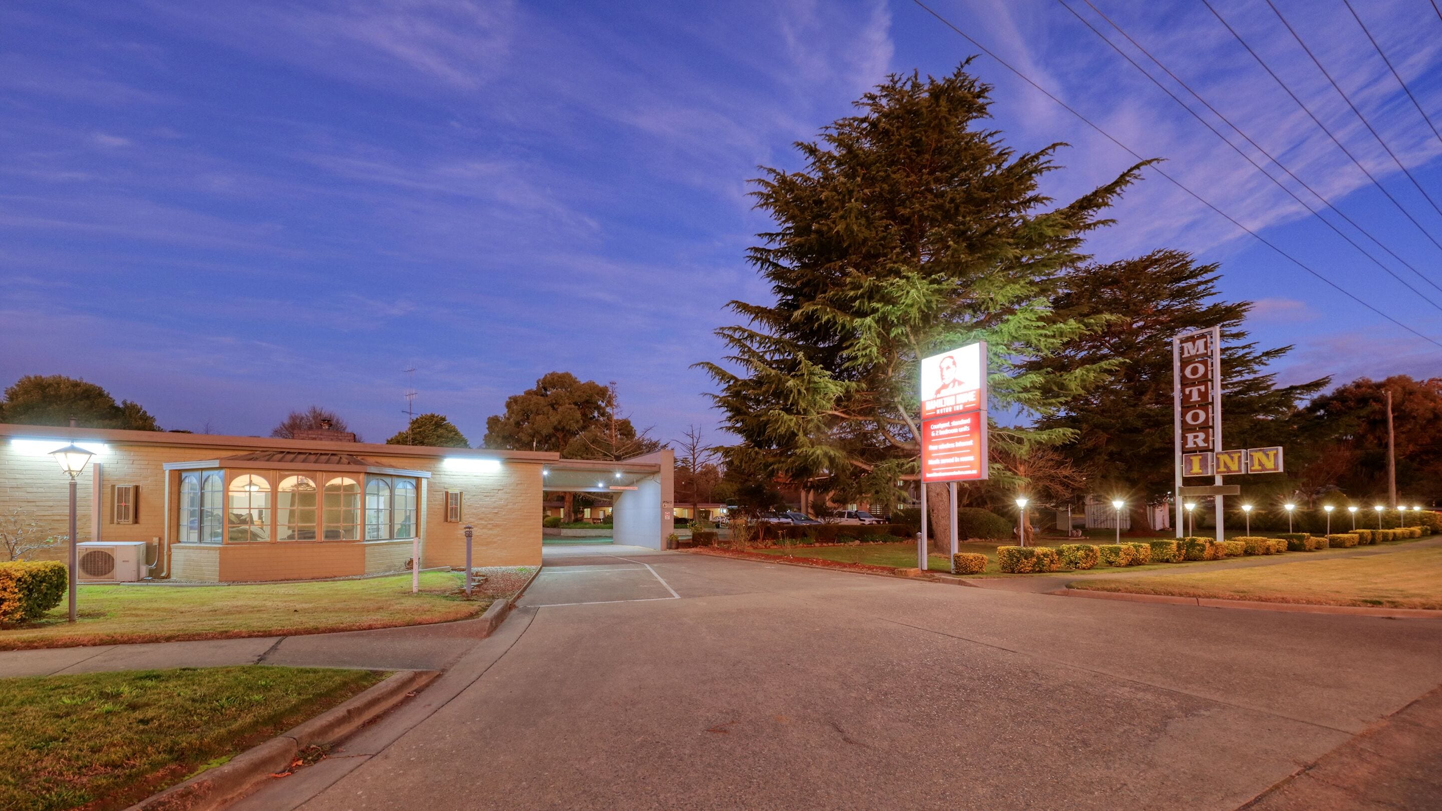 Un motel con un cartel, un área de estacionamiento y un edificio con entrada cubierta.