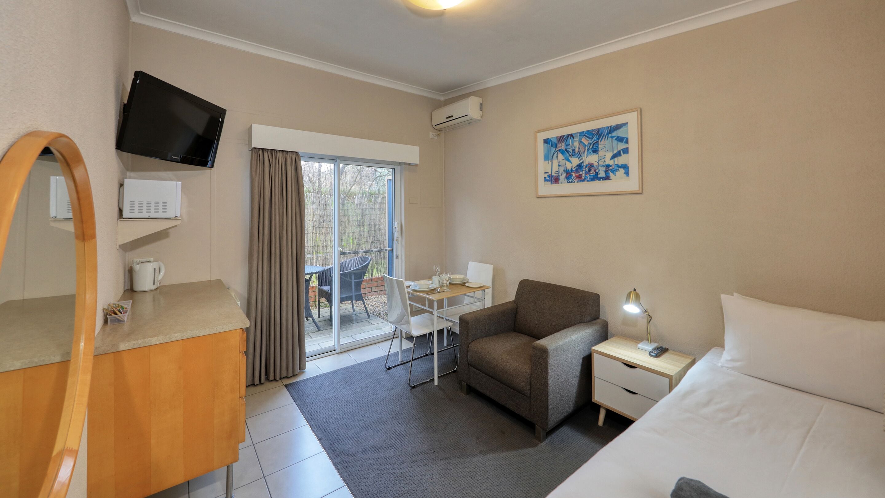 Une chambre d’hôtel avec un lit, un bureau et une chaise, une télévision, un tableau et une fenêtre avec des rideaux.