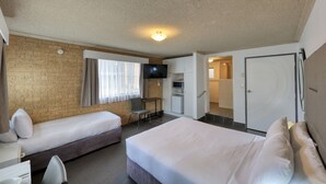 A hotel room with two beds, a TV, a desk, and a kitchenette.