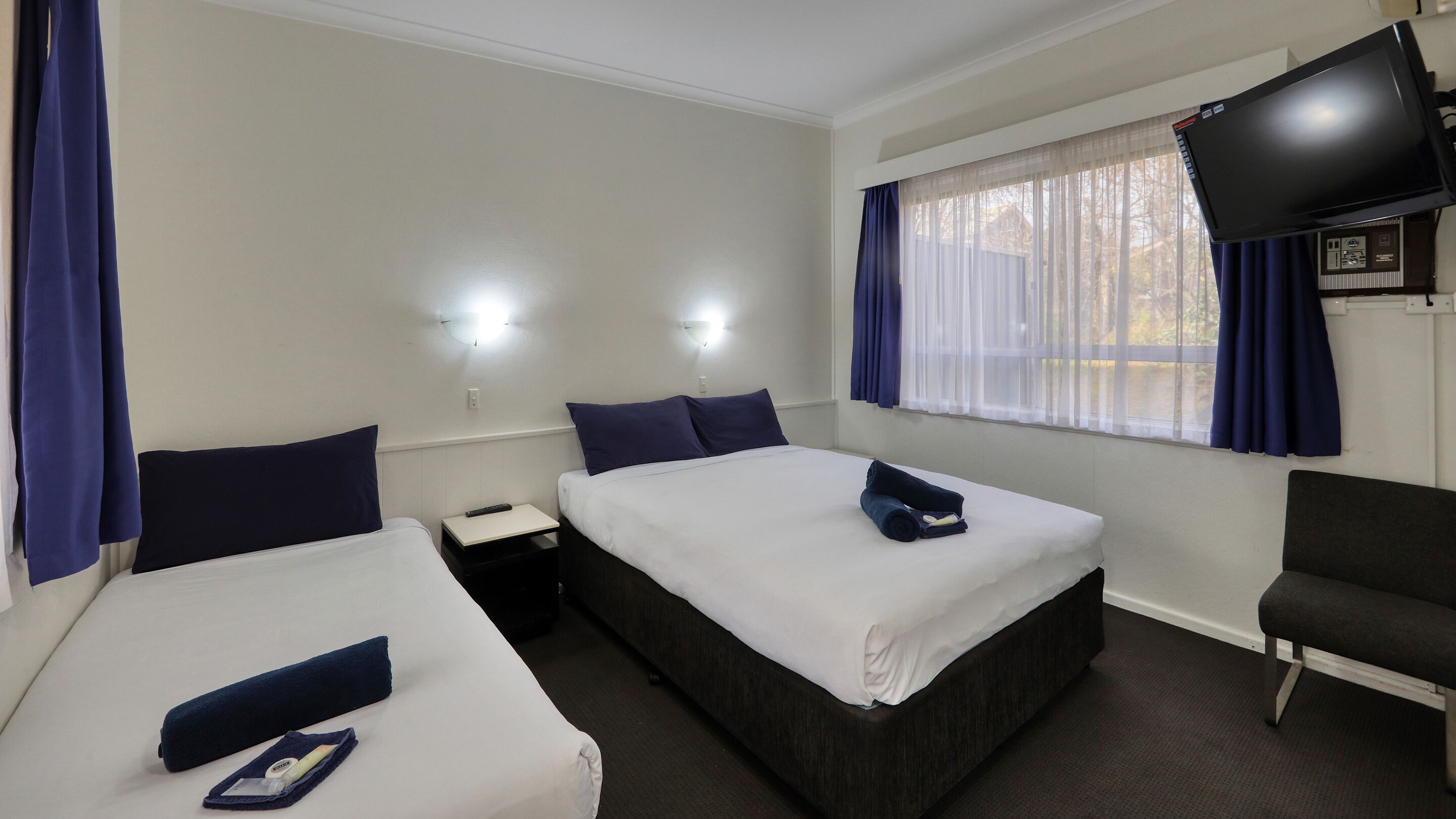 A hotel room with two beds, a TV, a chair, and a window with curtains.