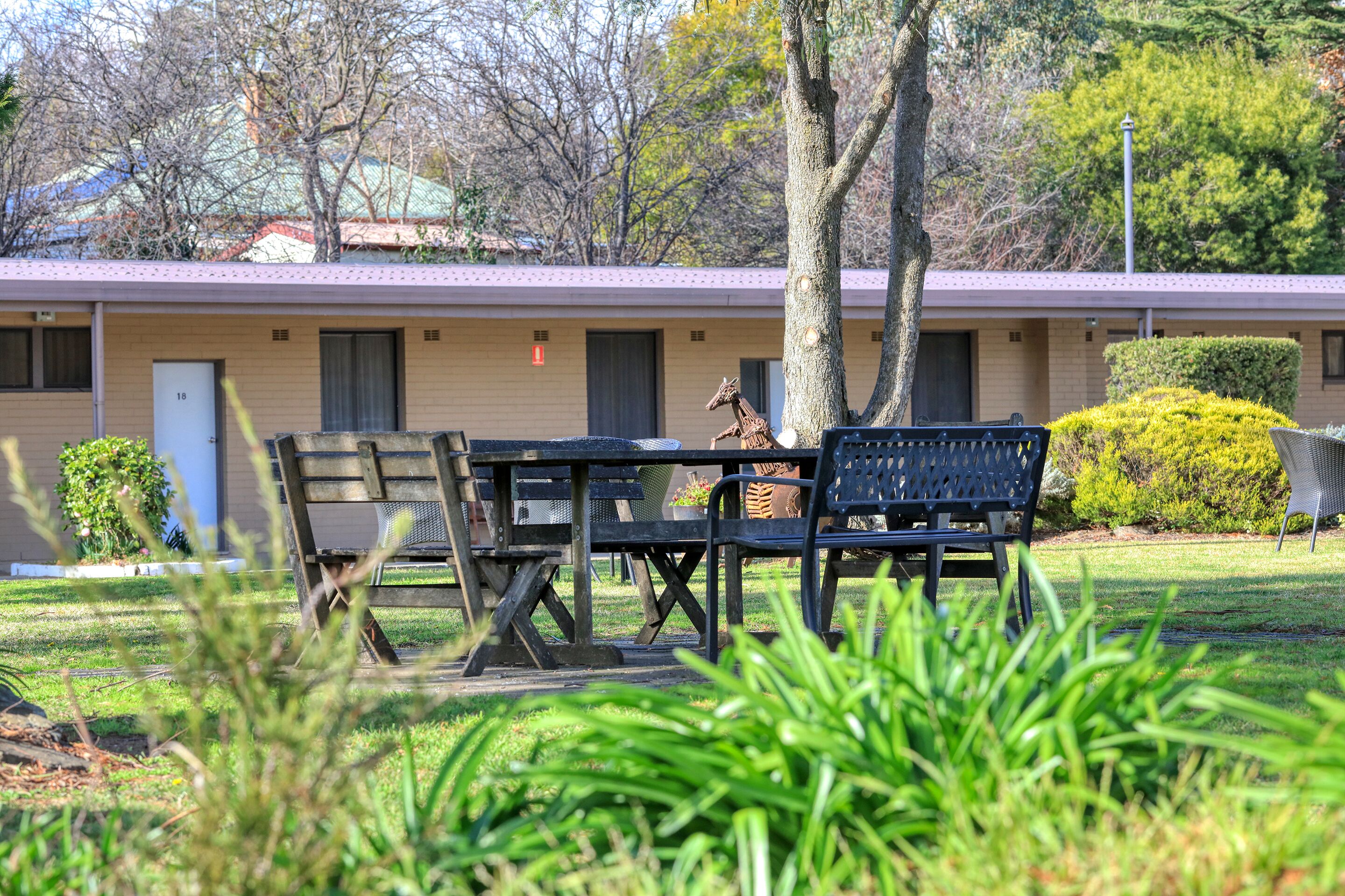 A motel with a patio area featuring a table and chairs, a giraffe statue, and a well-maintained lawn.