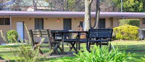 A motel with a patio area featuring a table and chairs, a giraffe statue, and a well-maintained lawn.