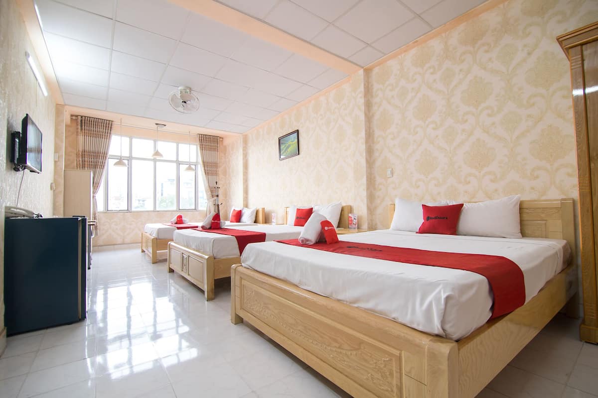Quarto de hotel com três camas de solteiro, uma escrivaninha e uma televisão.
