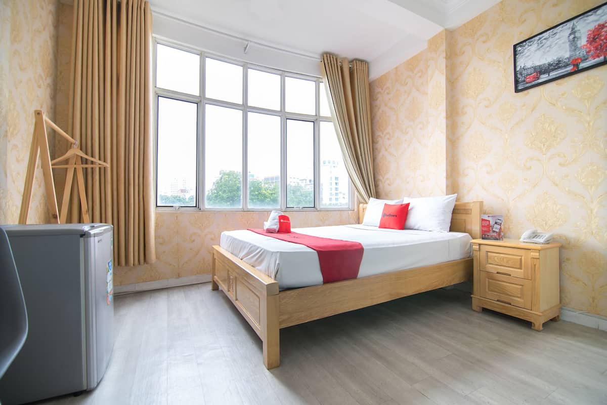 Quarto de hotel com cama, mesa de cabeceira, escrivaninha e janela com cortinas.