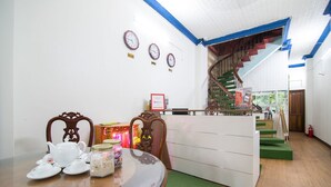 Un comedor con una mesa de madera, sillas y un armario blanco. Hay relojes en la pared y una escalera al fondo.