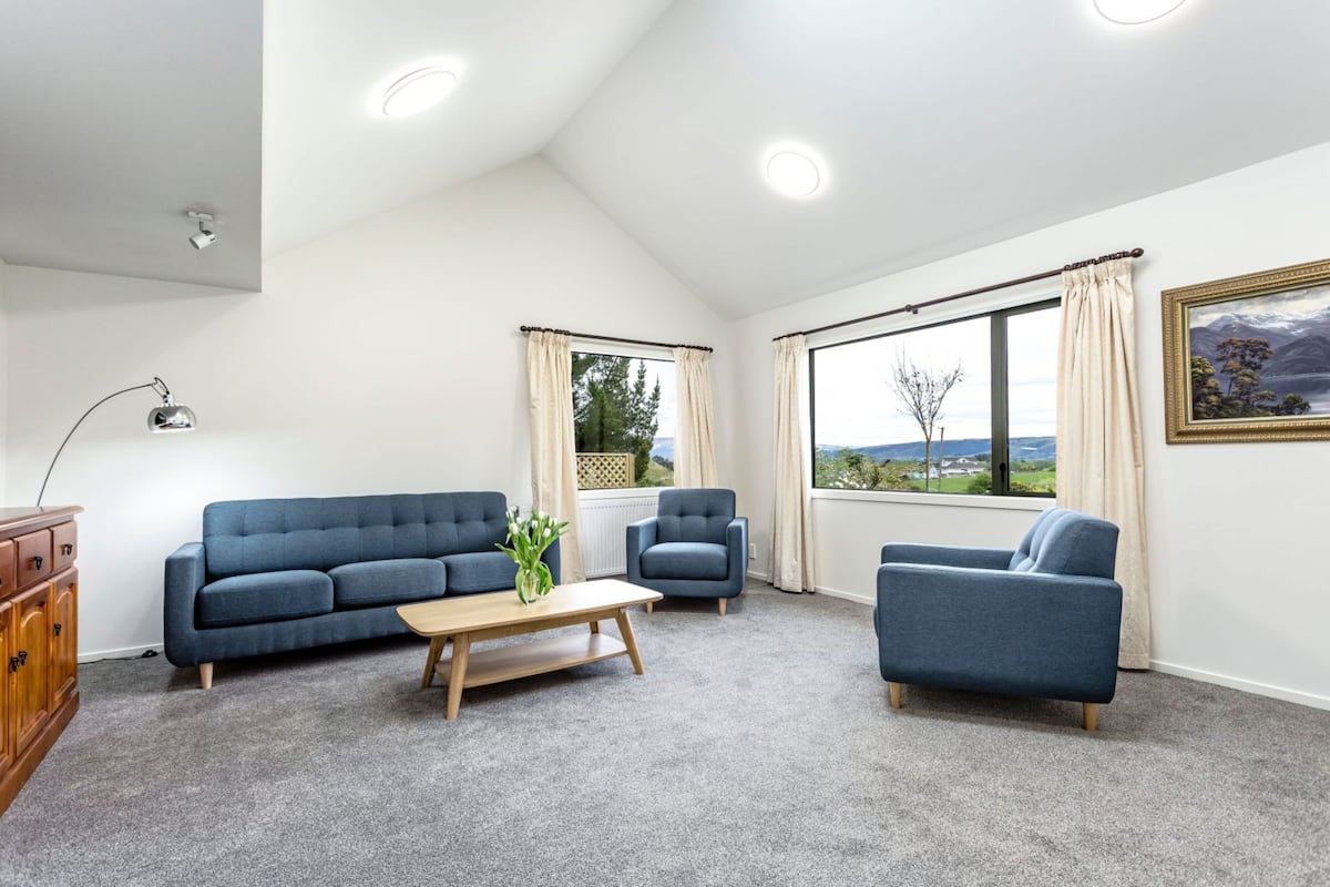 Una sala de estar moderna con un sofá azul, una mesa de centro de madera y vistas al exterior a través de amplios ventanales.
