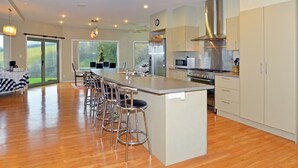 A modern kitchen with a central island, bar stools, stainless steel appliances, and a large window offering a view of the outdoors. - Hunters Moon (Mosgiel)