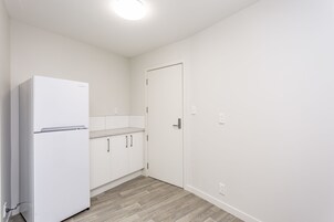 Una cocina pequeña y blanca con refrigerador, gabinetes de madera y una puerta blanca.