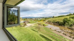 A window view of a rural landscape with a river, grassy fields, and distant houses. - Hunters Moon (Mosgiel)