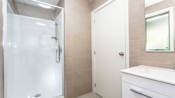 A modern bathroom with a glass-enclosed shower, a white vanity with a mirror, and beige tiled walls.