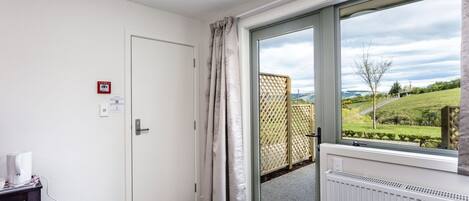 A room with a door, a radiator, a window with a view of greenery, and a small table with a tissue box.