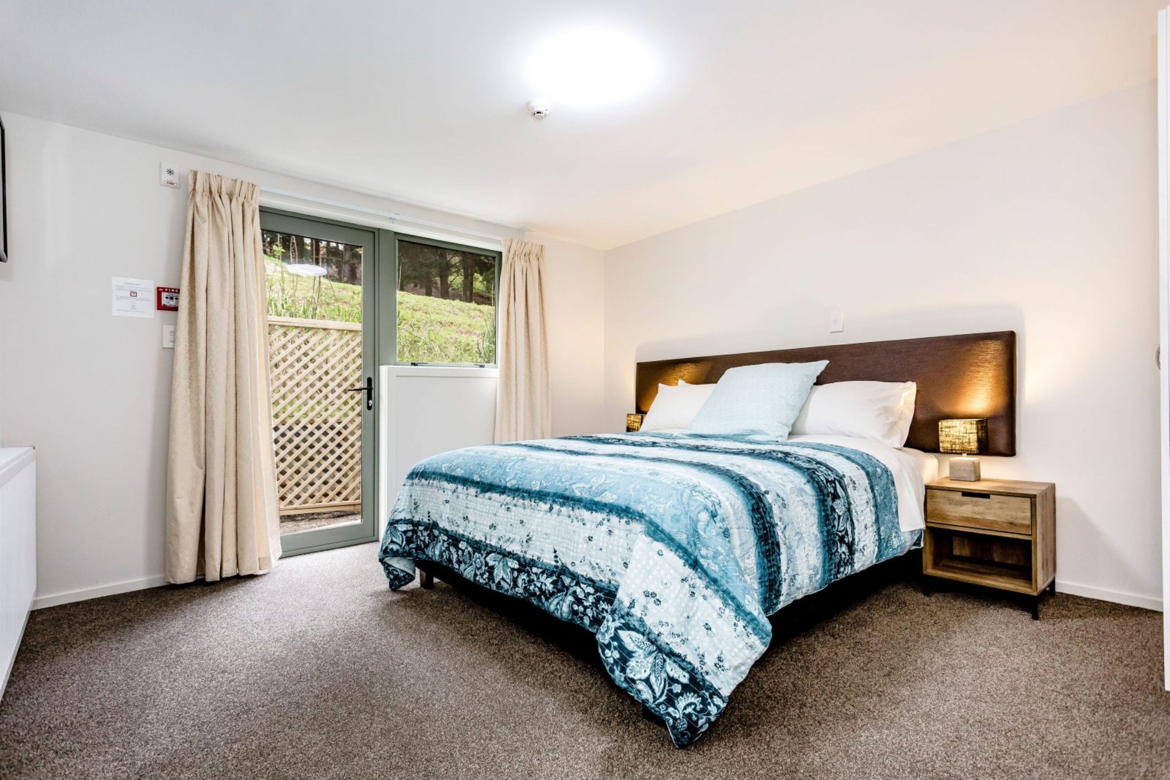 A bedroom with a bed, a nightstand, a lamp, and a sliding glass door leading to a balcony.