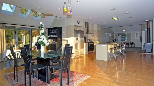 A spacious living area with a glass dining table, black chairs, and a red patterned rug. - Hunters Moon (Mosgiel)