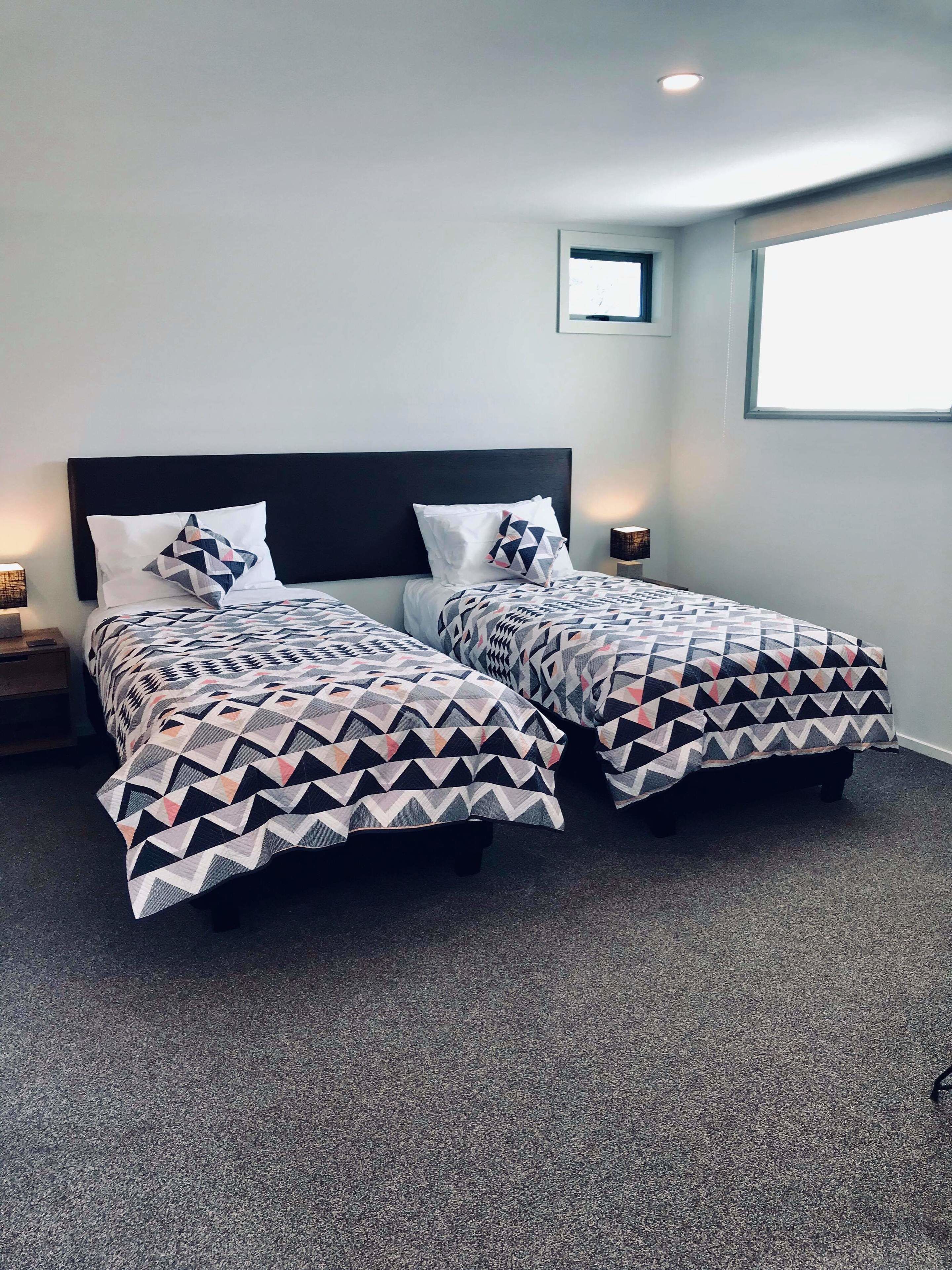 A hotel room with two beds, each with patterned bedding, a dark headboard, and a small bedside table with a lamp.