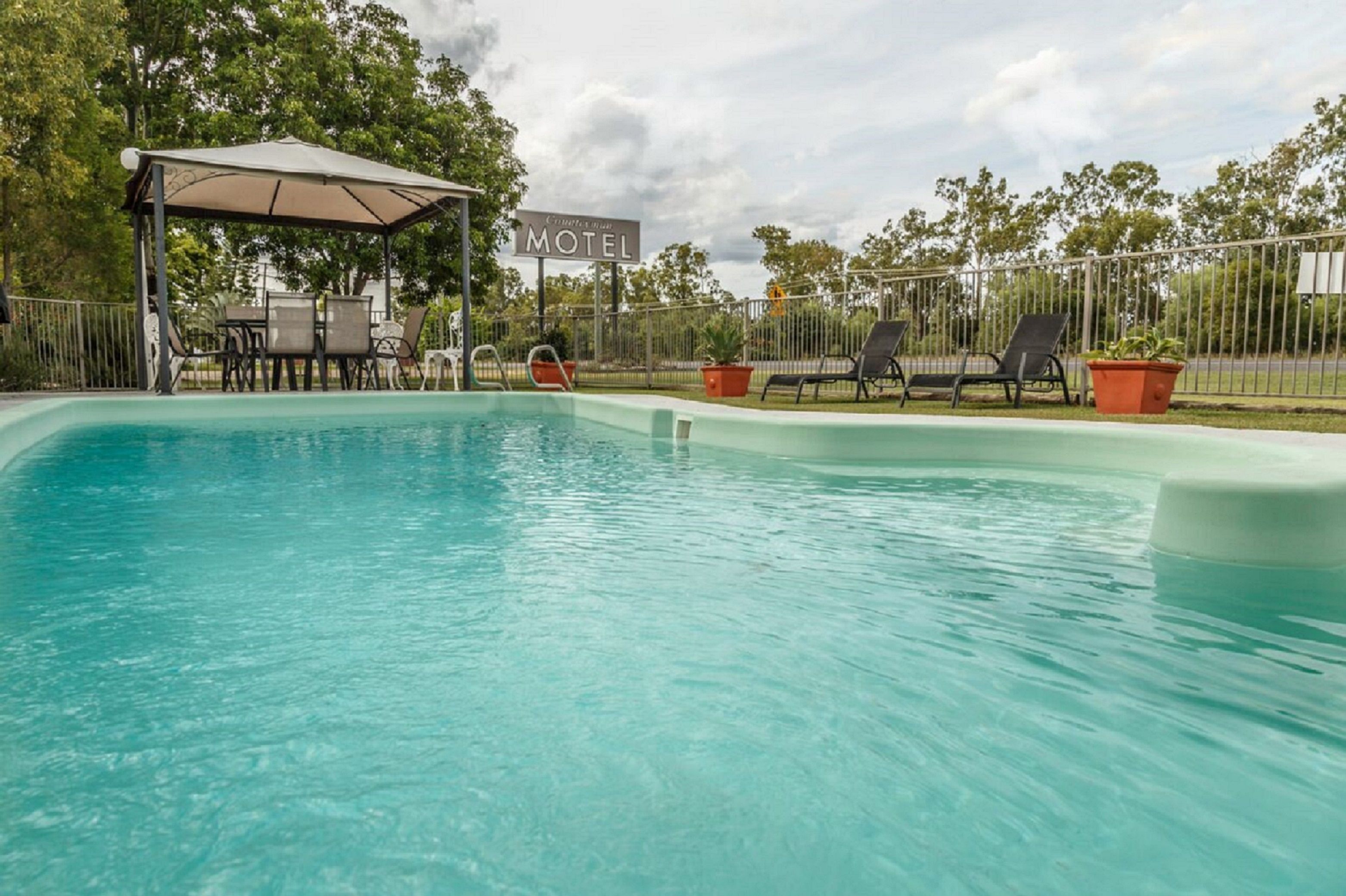A swimming pool with lounge chairs and a covered seating area. A sign indicates the presence of a motel nearby.