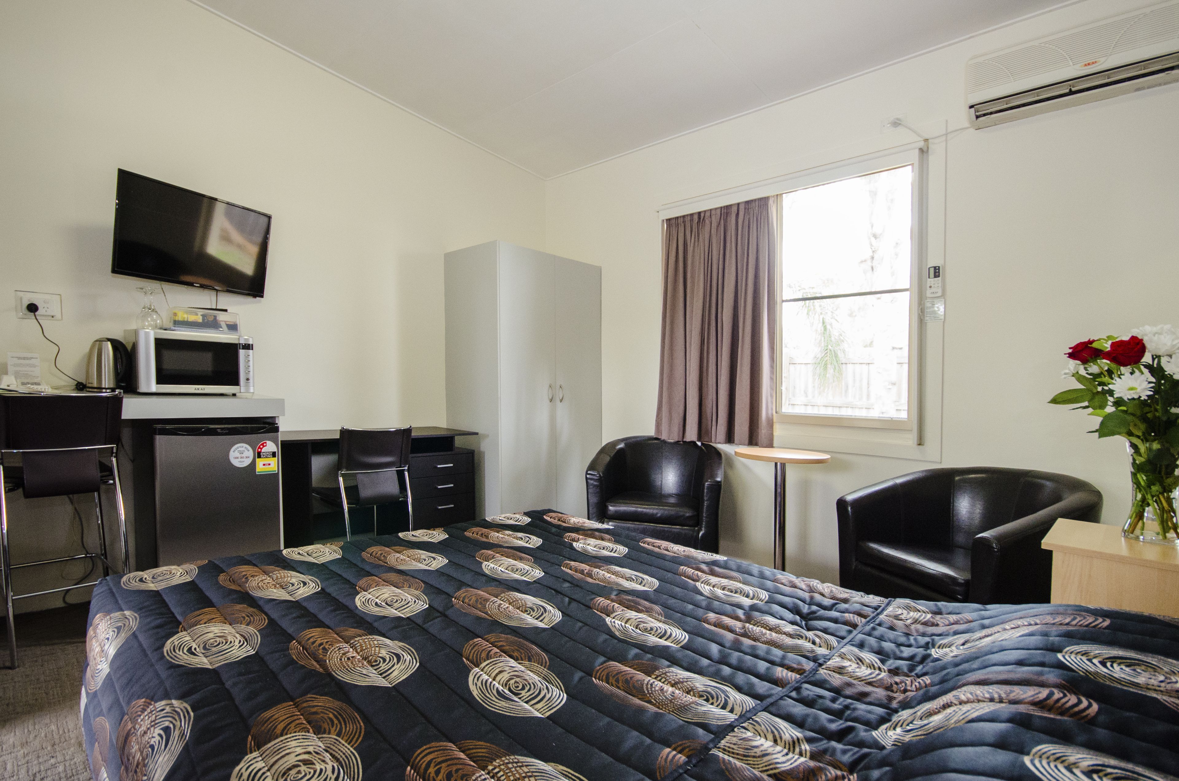 Habitación de hotel con cama, escritorio con microondas, televisión, silla y ventana con cortinas.