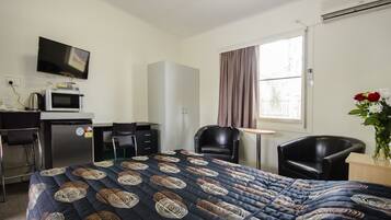 Habitación de hotel con cama, escritorio con microondas, televisión, silla y ventana con cortinas.