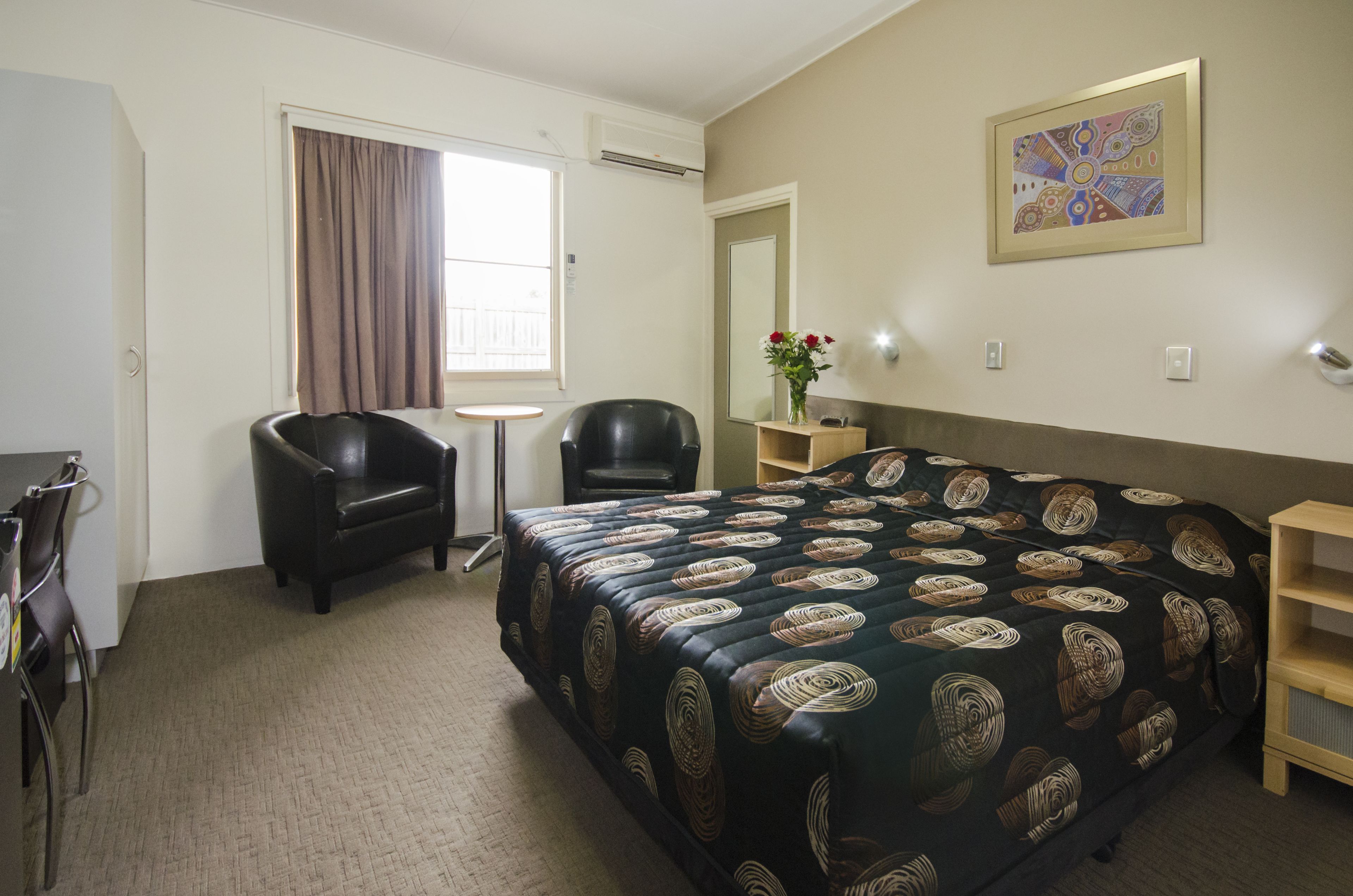 Habitación de hotel con cama, escritorio, silla, mesita y espejo.