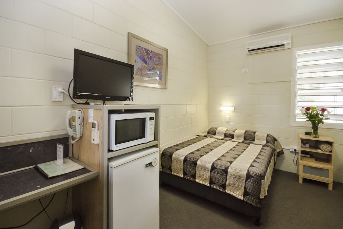 Une petite chambre propre, équipée d’un lit, d’un bureau avec un ordinateur, d’un four à micro-ondes et d’une télévision.