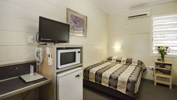 A small, clean room with a bed, a desk with a computer, a microwave, and a television.
