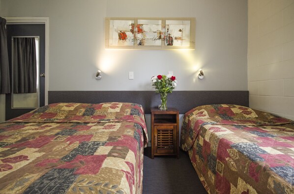 A hotel room with two beds, a small table with a vase of flowers, and a wall-mounted artwork. - Biloela Countryman Motel (Biloela)