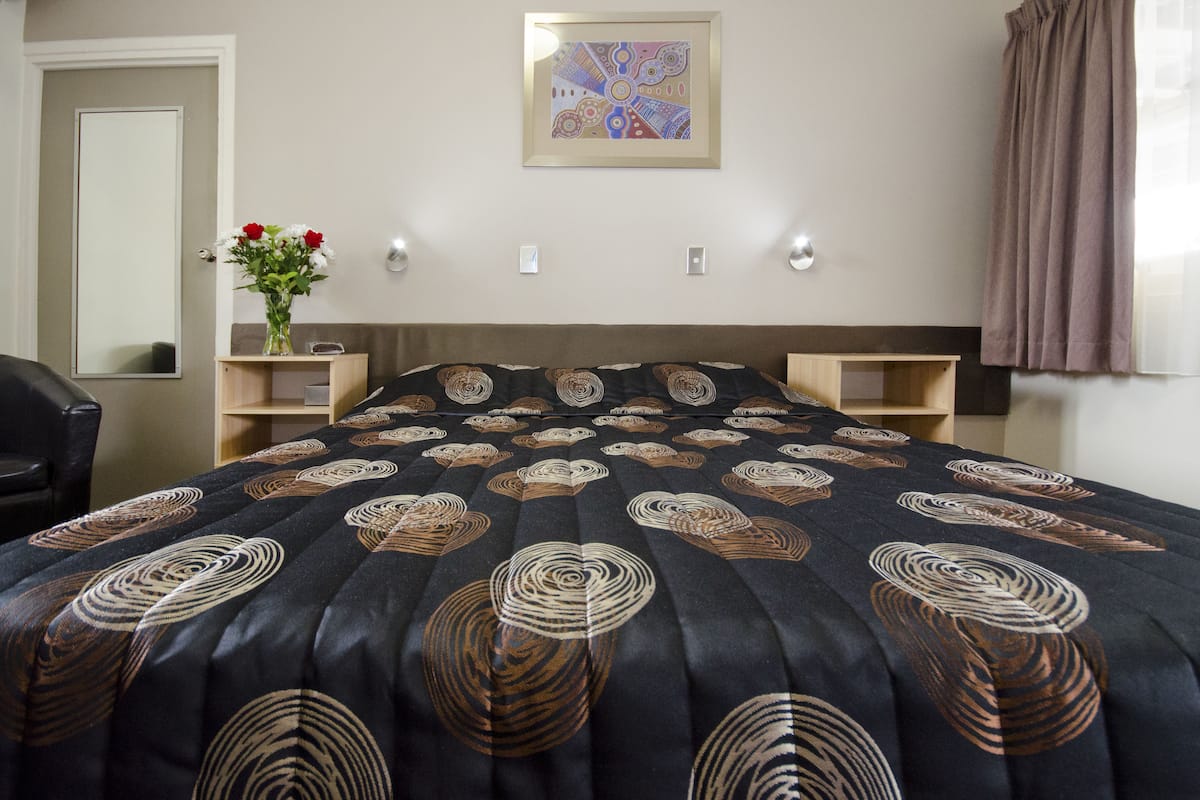Une chambre d’hôtel avec un grand lit, une table de chevet, un miroir et une œuvre d’art accrochée au mur.